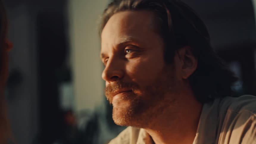 The video begins with a closeup of a man tenderly kissing a womans forehead eyes closed in the momenthe then looks up with a warm gentle smile his expression conveying deep affection