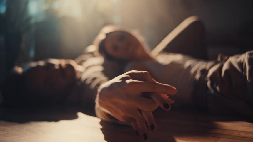 Couple lying on the floor with interlocked hands under soft light coming through the window