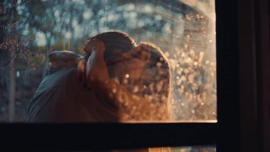 Couple embracing near a wet window under warm external light