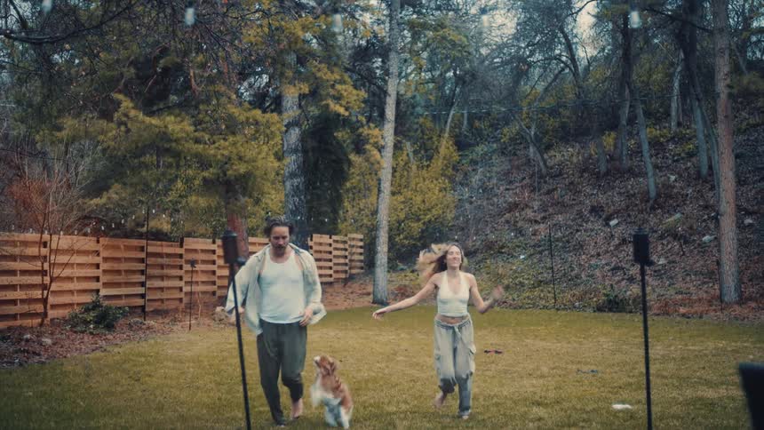 Couple running on the lawn with a dog in a yard surrounded by trees