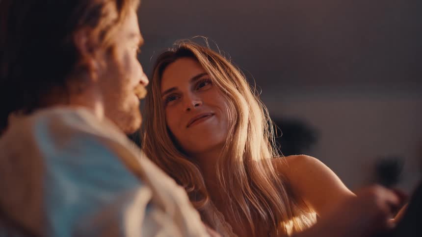 A young couple sit indoors at midday smiling at each other as they have a discussion