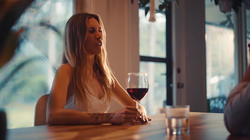 Woman smiling while holding a glass of wine seated at a table in a welllit setting