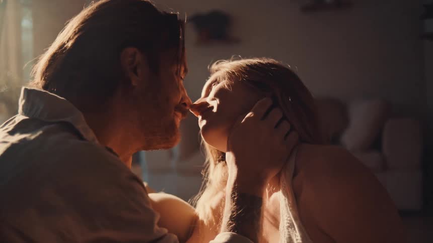 Couple shares tender kiss in softly lit indoor setting with intimate atmosphere