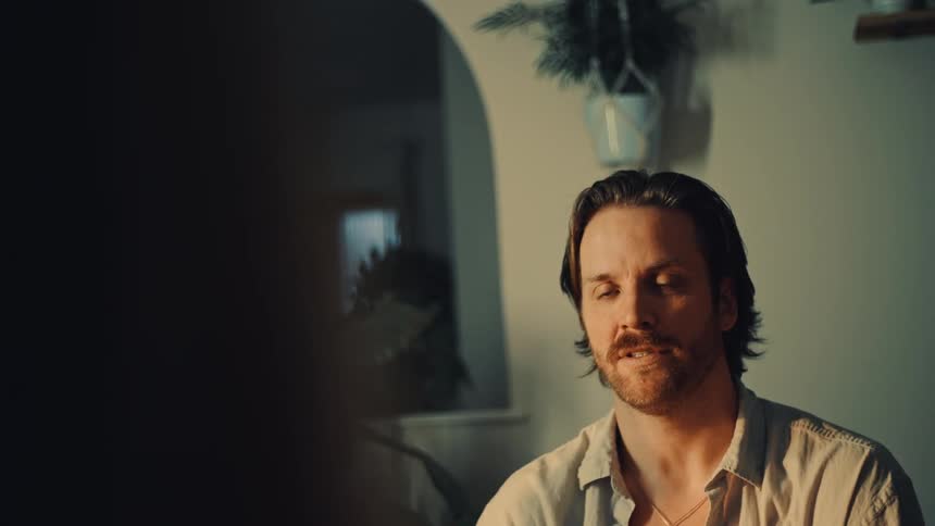 A bearded man nods and talks earnestly during a conversation in a dimly lit room