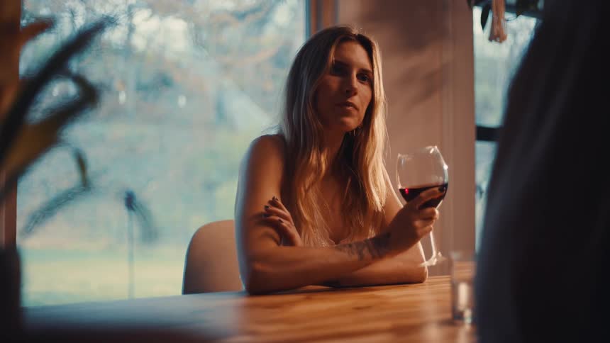 Woman holding a glass of wine while sitting at a table near a bright window