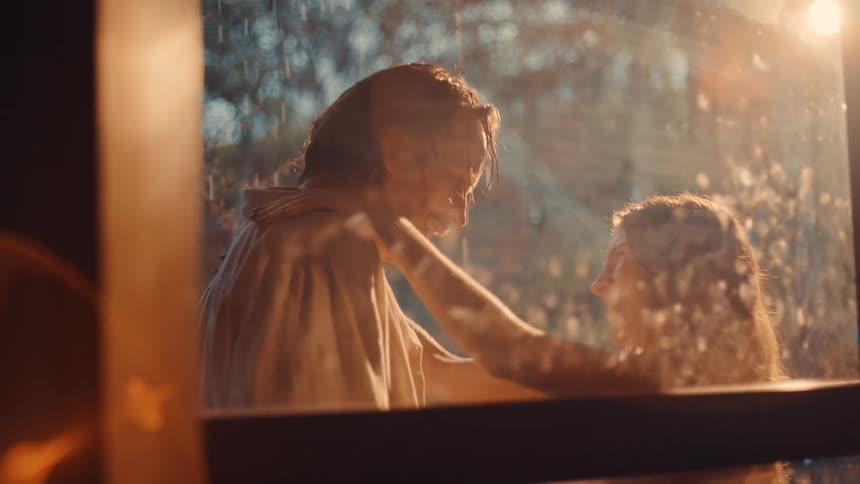 A young couple walk to the balcony from the rain hugging each other while wet as sunlight shines on them they laugh and stare at each other