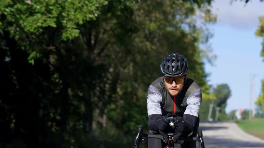 Cyclist wearing a helmet and sunglasses riding on a treelined road