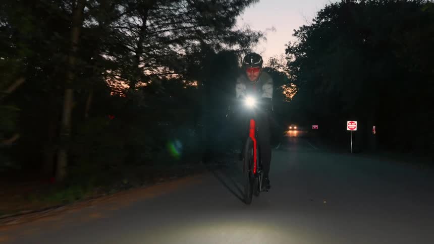 Cyclist riding at night with a headlight on along a treelined road