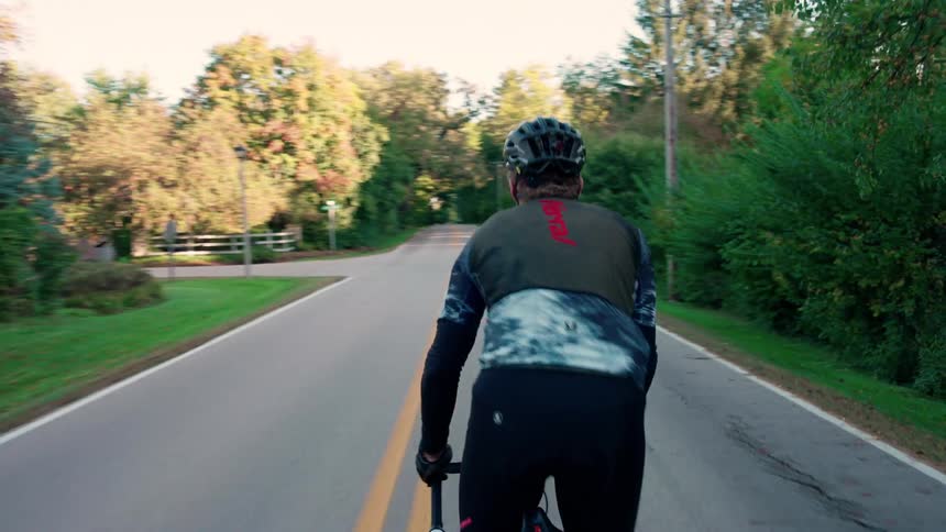 A young man wearing a helmet cycles in the middle of a rural road at midday