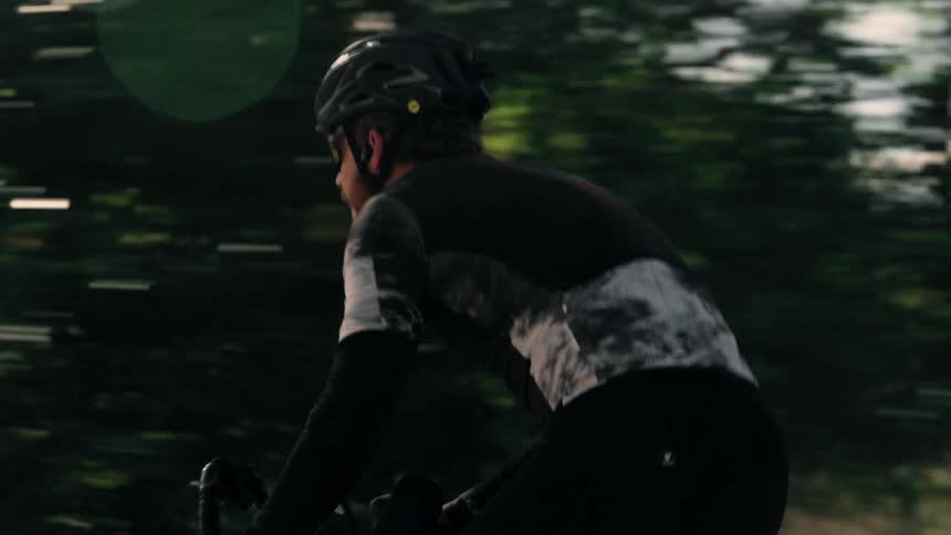 A cyclist wearing dark athletic gear and a helmet is shown in a tight shot from behind and the side as they ridethe background blurs past rapidly due to motion highlighting the speed and focus of the rider