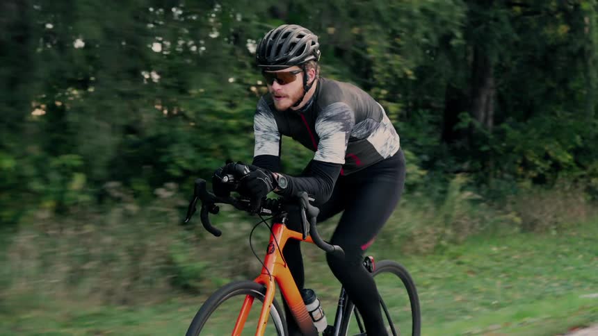 The video shows a male cyclist riding a road bike outdoorshe is wearing cycling gear including a helmet sunglasses gloves and a longsleeved jersey suggesting he is training or riding in cool weather