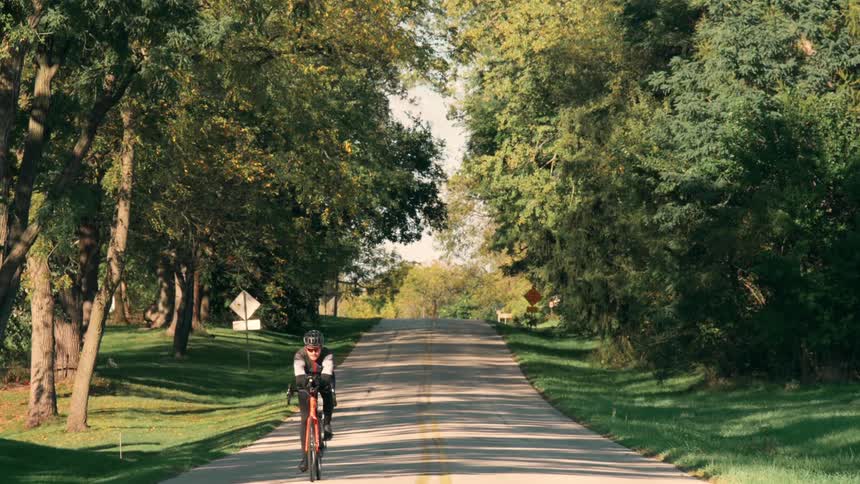 The cyclist moves fast past the trees on the road
