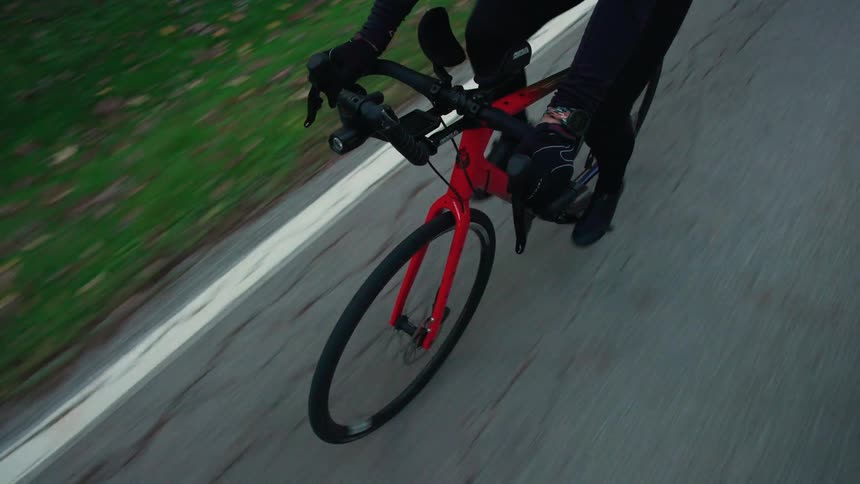 A person wearing a black tracksuit cycles along the side of the road at midday