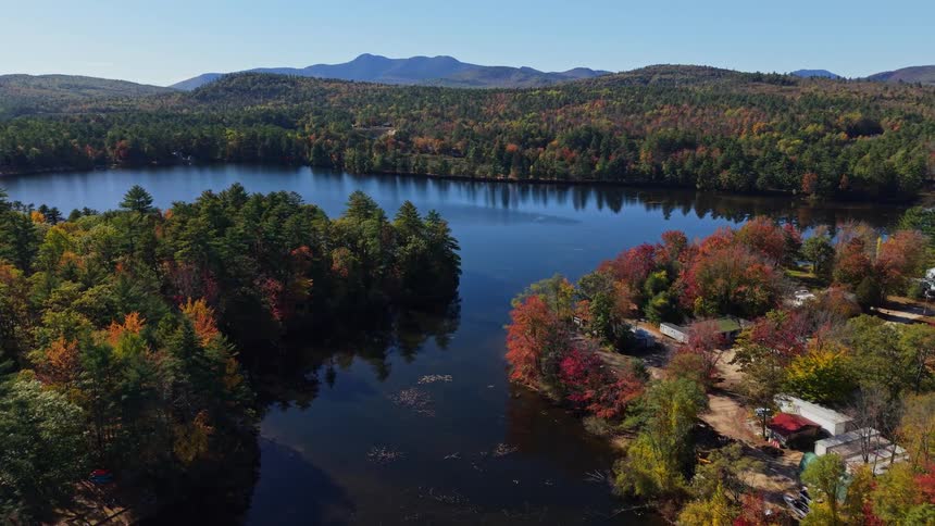 Houses in a neighborhood on the coast of a forested lake with trees in bright fall colors and mountains in the distance