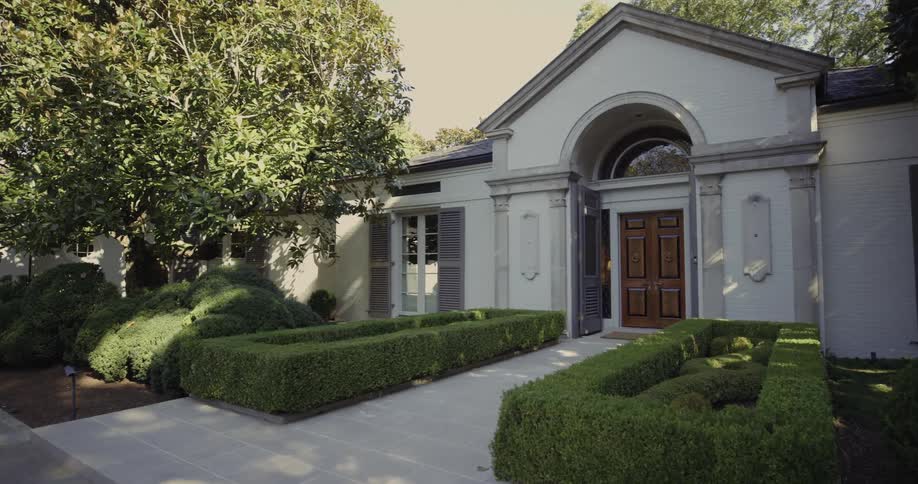 Shaped hedges line the walkway leading to the wooden doors of a large house