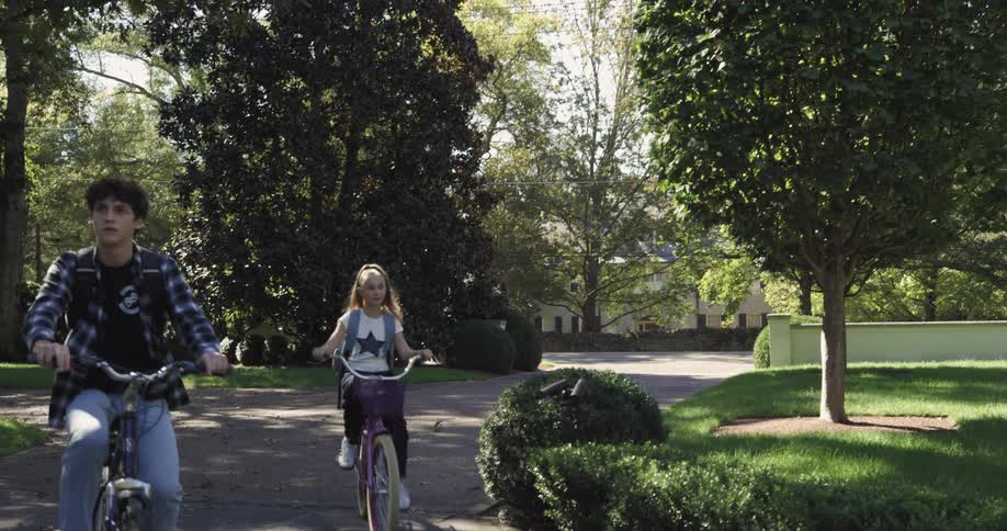 A male and female teenager ride bicycles and stop on a path outdoors during daytime