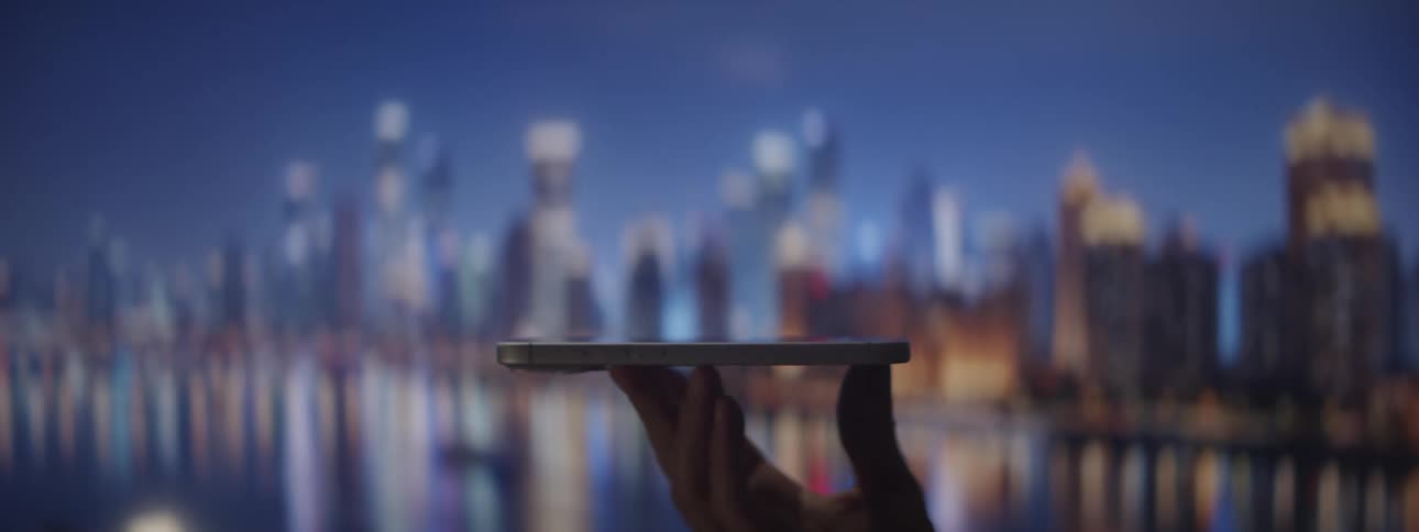 Hand holds electronic device in front of lit city with reflections on water