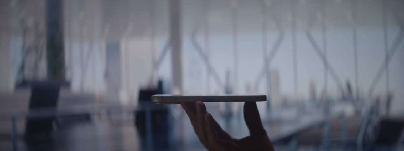 Hand holds tablet in modern office setting with large windows and natural light