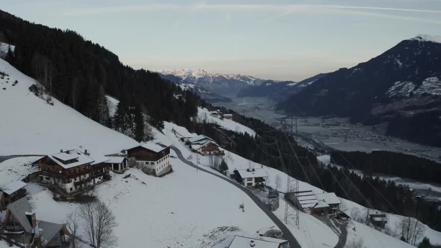 Snowcovered houses line winding road between dense forest and distant mountains