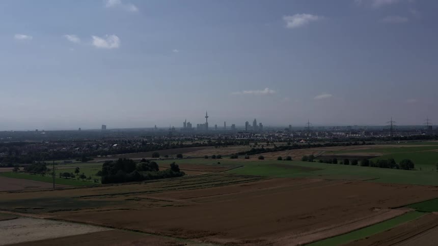 Agricultural fields stretch toward urban skyline with central telecommunications tower