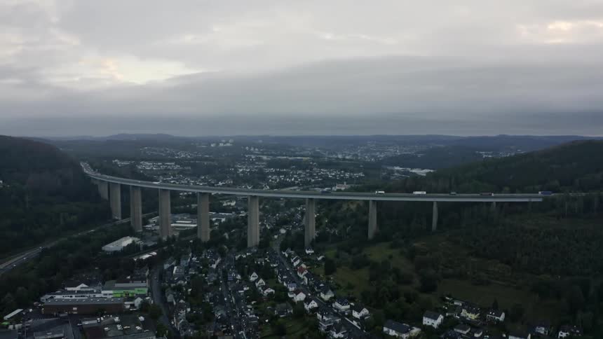 Traffic moves along a raised highway passing over a residential neighborhood located between hills on an overcast day