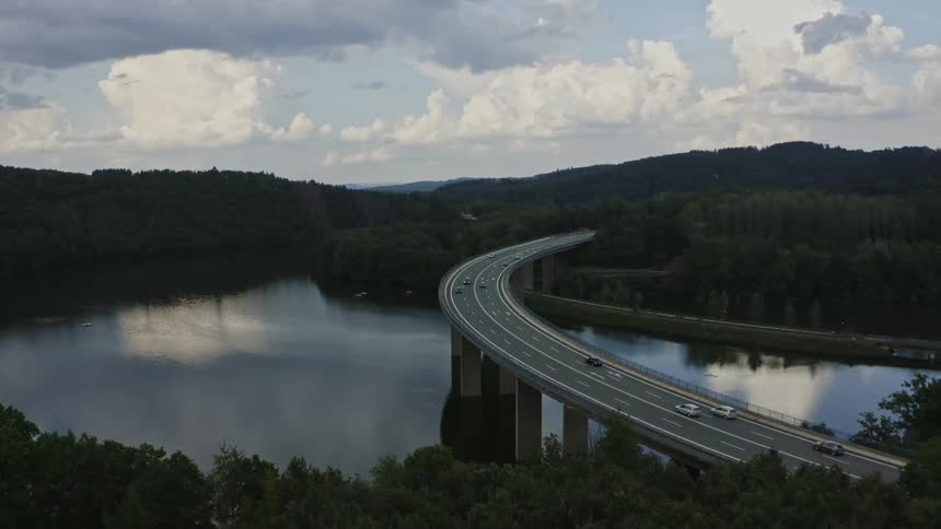 Curved overpass spans water body amid densely forested hills