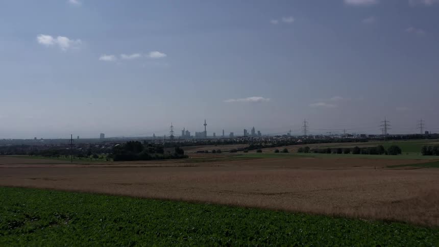 Moving over a field with utility towers and traffic on the highway with buildings in the distance