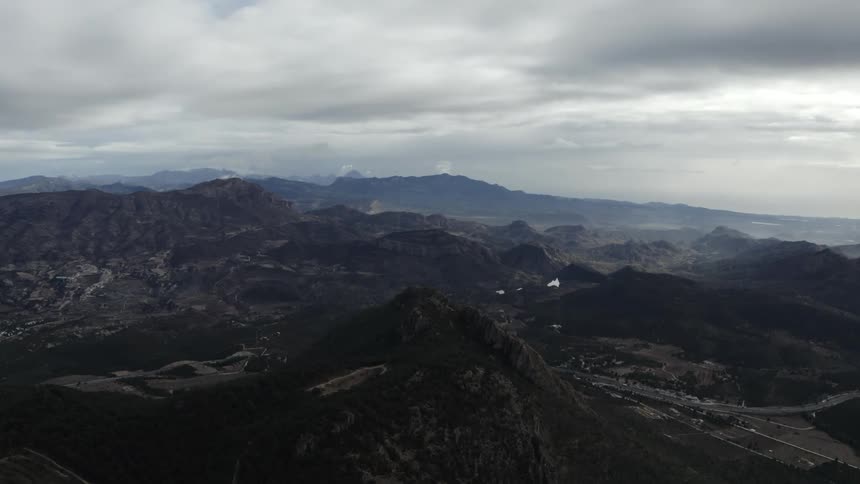 The video shows a wide static aerial view of a rugged dark mountain range under a cloudy sky a winding highway is visible in the lower right and a filmsupply watermark is present across the center