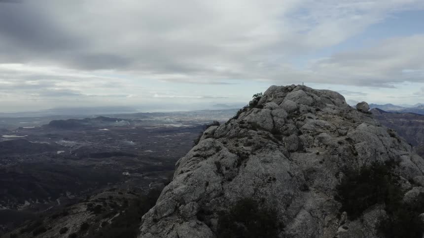 Rocky peak overlooks mountainous terrain with sparse vegetation under partly cloudy sky