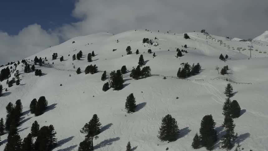 The video is an aerial shot of a snowcovered mountainside it shows scattered pine trees and evidence of skiing or snowboarding tracks on the slopes with a chairlift visible in the distance on the right side