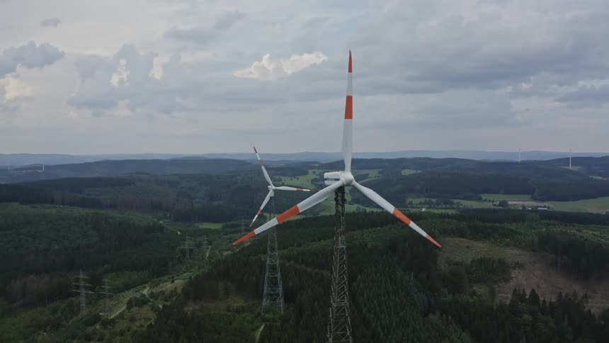 Aerial view of turbines spinning on a wind farm on a forested mountain