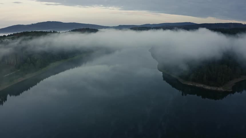 Water reflects a tower and the waterside forests on a foggy autumn day