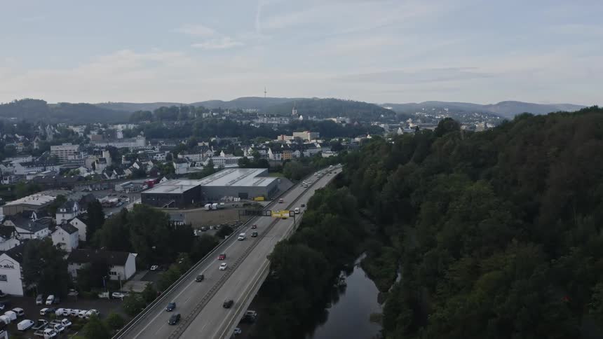 An aerial view shows traffic flowing along a highway that separates a town from a dense forest and river