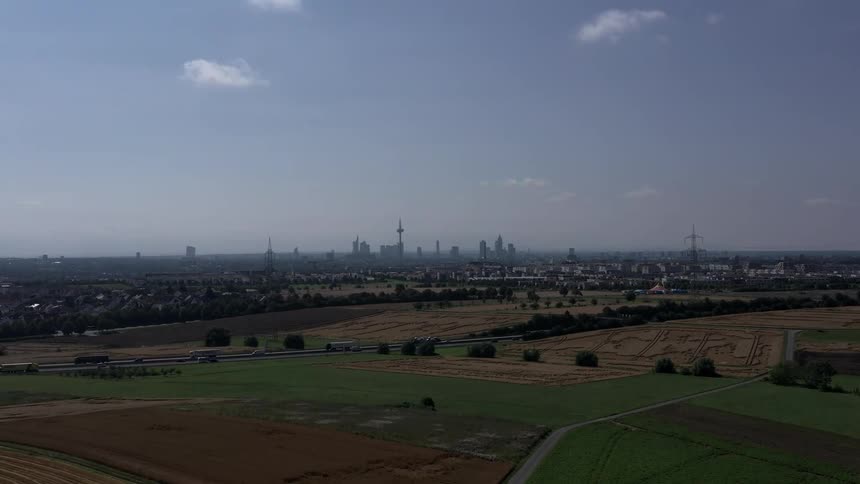 Daytime aerial landscape shows farmland with a highway in front of an urban area