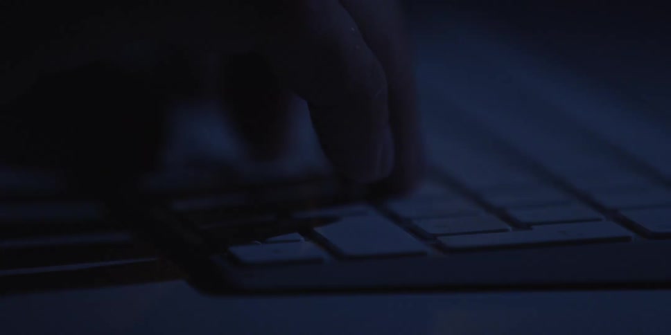 Closeup of a hand typing on a keyboard in a dark workspace
