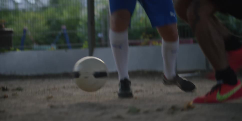Soccer ball rolls on the ground as players contest the play on an outdoor court