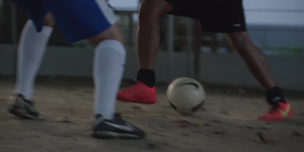 Players contest ball on sandy ground with red and black cleats in motion