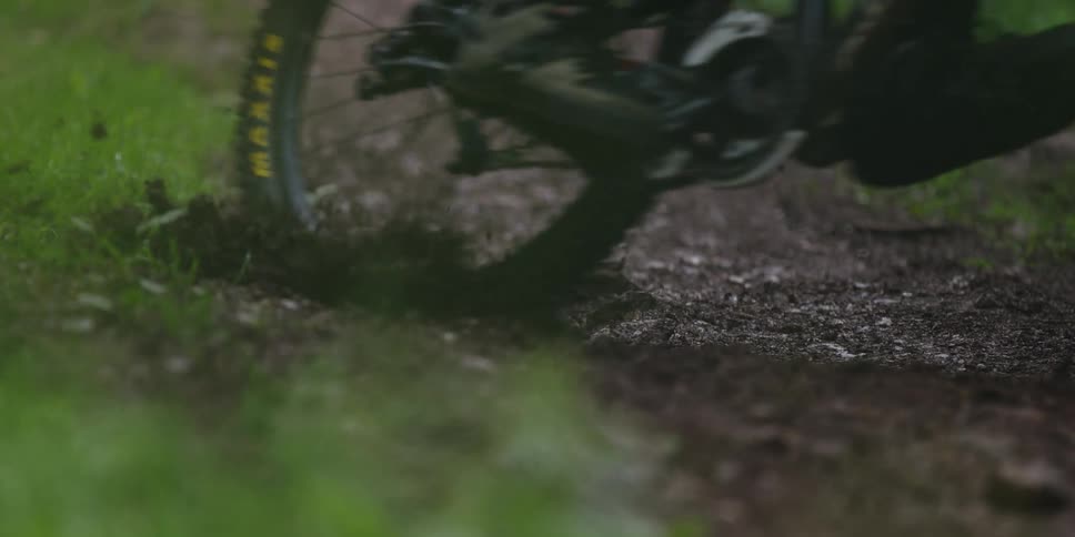 Bicycle rides through muddy trail in forested area with splashes of water and dirt in motion