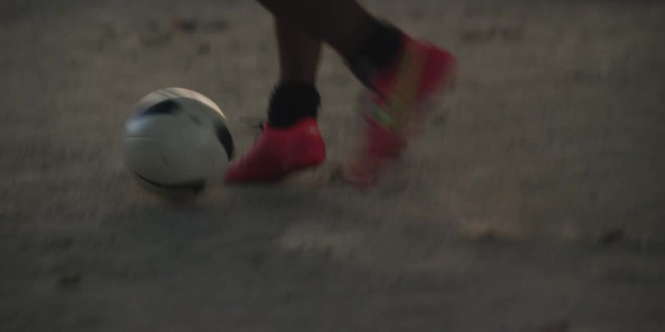 The soccer players move the ball across the dirt
