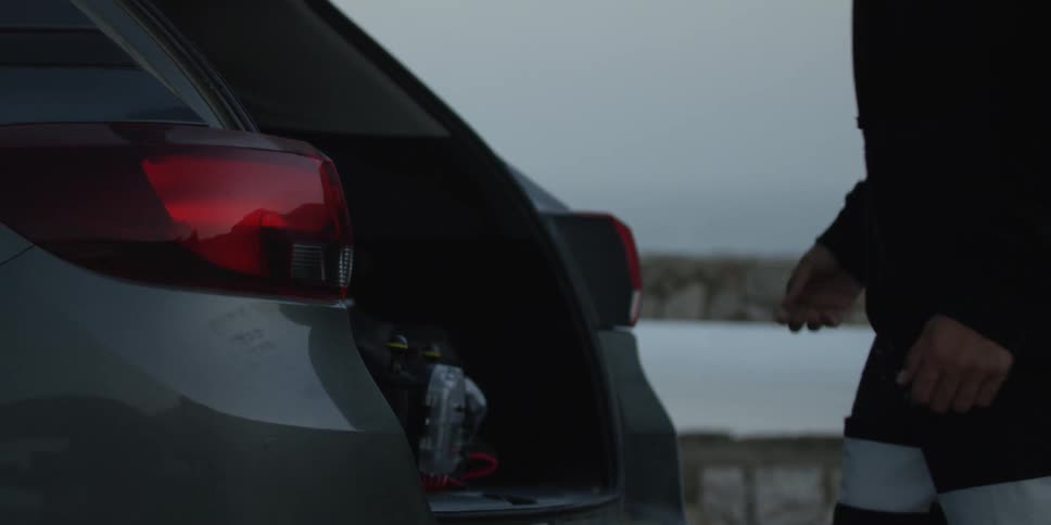 A person opens the trunk of a car and takes an item out at midday
