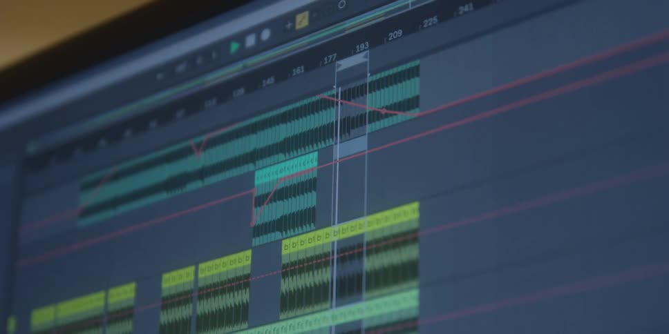 A closeup shot of a computer screen shows a digital audio workstation software interface with green and yellow audio waveforms as a red automation line scrolls across the tracks and timeline