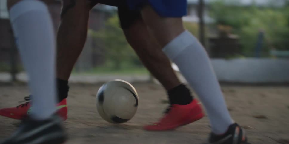 Two players tussle for control of the soccer ball on a dirt field