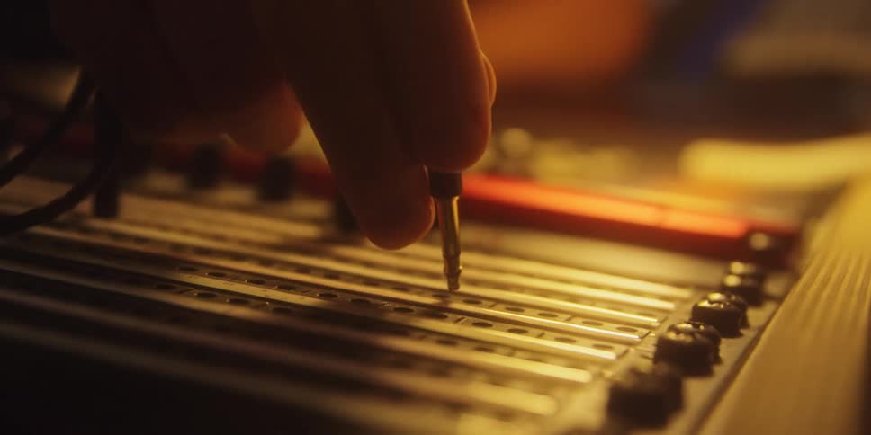 Hand plugging a cable into audio equipment under warm ambient light