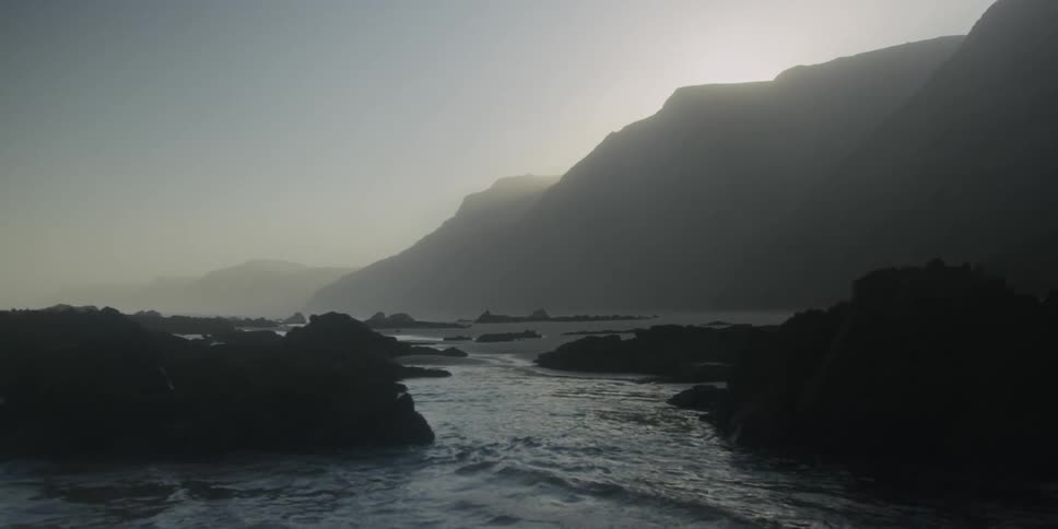 Ocean water gently washes ashore upon a mountainous coastline