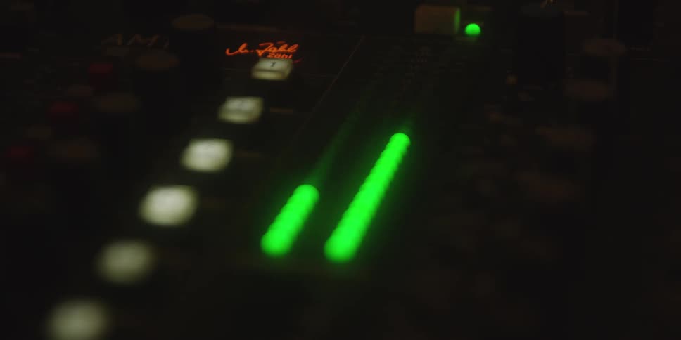 Closeup of a sound mixer panel with glowing green and red audio level leds