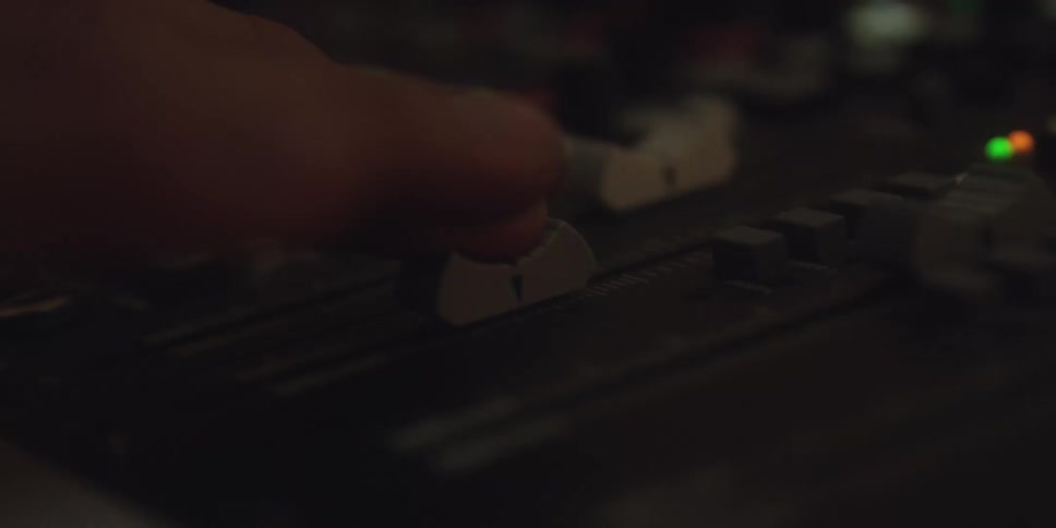 The video shows a closeup shot of a hand adjusting a fader or slider on an audio mixing board or sound console in a dimly lit environment the finger pushes the slider up and down slightly suggesting finetuning of an audio level or effect