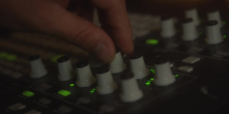 Closeup of a hand adjusting audio knobs on a dimly lit sound mixer in a studio
