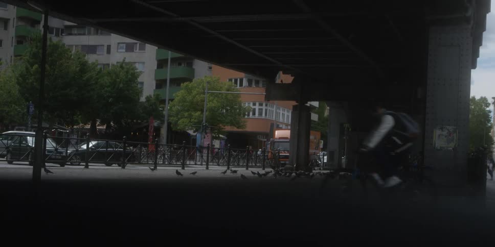 Pedestrians walking under an overpass while a cyclist with an orange backpack passes by