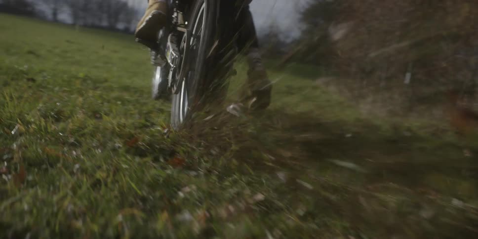 From a lowangle closeup a dirt bikes rear wheel digs into the ground kicking up mud and grass as it accelerates rapidly across a field