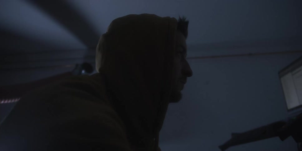 Hooded person working in front of a monitor in a dark environment